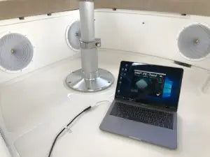Laptop on a white surface with speakers and a monitor in the background